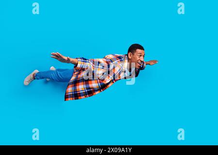 Full size photo of nice young man flying empty space wear shirt isolated on blue color background Stock Photo