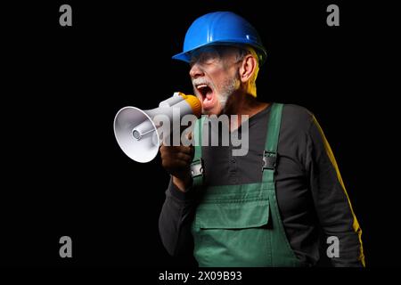 Mature miner man shouting into megaphone on black background Stock Photo