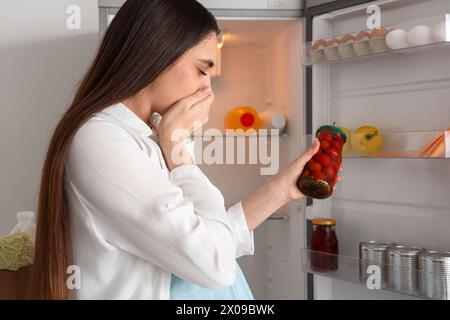 Young pregnant woman feeling bad smell from canned tomatoes near fridge in kitchen Stock Photo