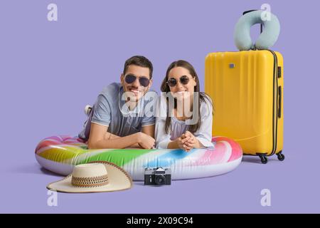Beautiful young happy couple of tourists with suitcase, inflatable mattress and camera on purple background Stock Photo