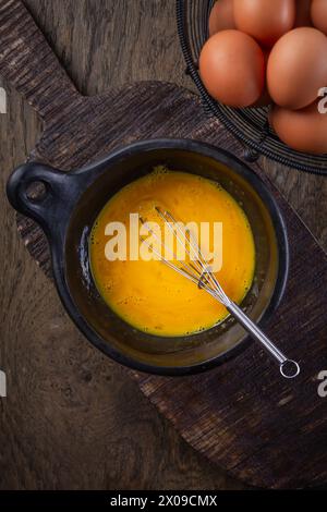 Organic whipped eggs in black bowl with whisk, cooking preparation Stock Photo