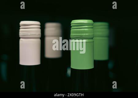 assorted wine bottles with colorful labels, each adorned with vibrant green and pink caps on shelves, providing a festive holiday atmosphere for wine Stock Photo
