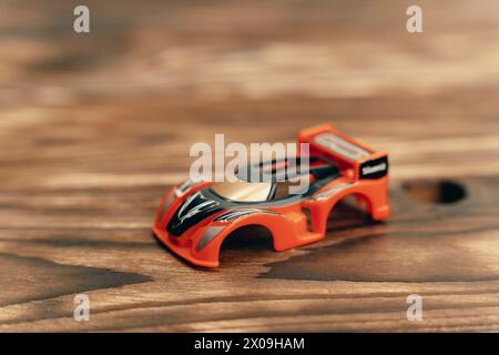 A small toy car is parked on top of a wooden table, showcasing its vibrant colors against the natural wood grain. Stock Photo
