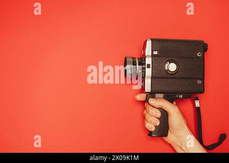 vintage portable movie camera in a woman's hand on a red background. retro, 70s, 80s. Stock Photo