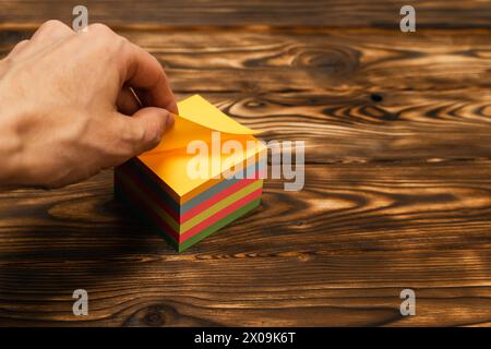 A hand tears off a colored sticker to record reminders. A block of paper for writing. self-adhesive stickers for notes, diary, laptop stickers, refrig Stock Photo