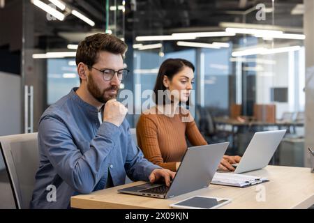 Two focused professionals working together at a desk with laptops in a contemporary office setting, conveying collaboration and teamwork. Stock Photo
