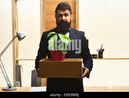 Frustrated employee leaving office with box of his belongings. Getting fired. Bearded businessman in suit with box of his stuff. Last day at work Stock Photo