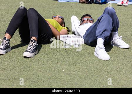 Atlanta, GA / USA - April 8, 2024:  Two teens lie on the ground and look through special glasses to view the total solar eclipse on April 8, 2024. Stock Photo