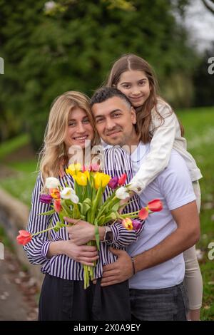 Happy family hugging in park, smiling and enjoying time together Stock Photo
