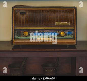 A classic, art deco style radio sits on a rustic wooden shelf. The radio is in good condition with a polished wood cabinet and a metal tuner. Stock Photo