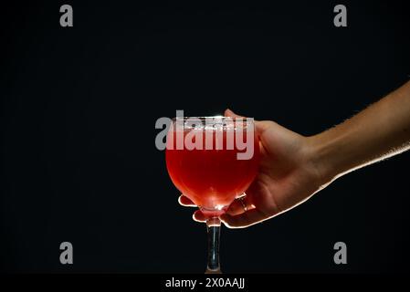 A right hand holding a glass cup with guava juice inside. Isolated on dark background. Stock Photo