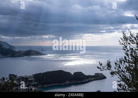 Natural light rays and blue cloudy sky over sea. Sunbeams reflections on calm sea water Corfu Greece. Seashore with a rays of sun against a moody dram Stock Photo