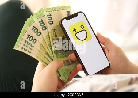 KYIV, UKRAINE - APRIL 1, 2024 Hago icon on smartphone screen and money in female hand. iPhone display with app logo and hundred euro bills in girls hands close up Stock Photo