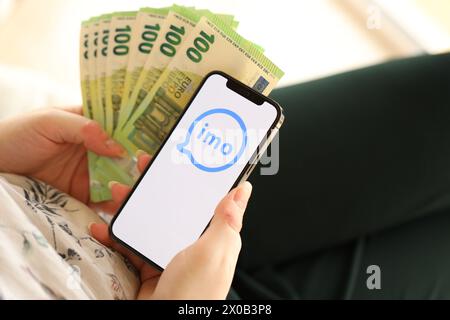 KYIV, UKRAINE - APRIL 1, 2024 Imo messenger icon on smartphone screen and money in female hand. iPhone display with app logo and hundred euro bills in girls hands close up Stock Photo