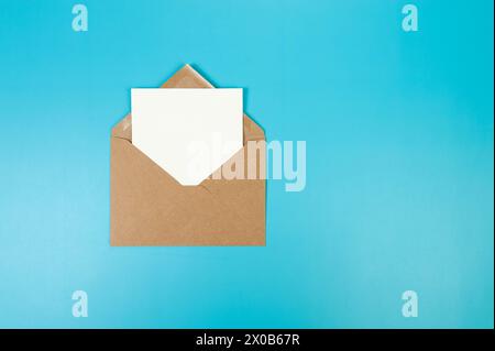Top view of brown Kraft envelope, white card on blue background. Post flat lay. Copy space. Stock Photo