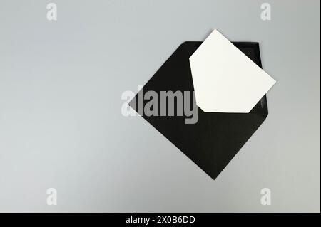 Top view of black envelope, white card on grey background. Post flat lay. Copy space. Stock Photo