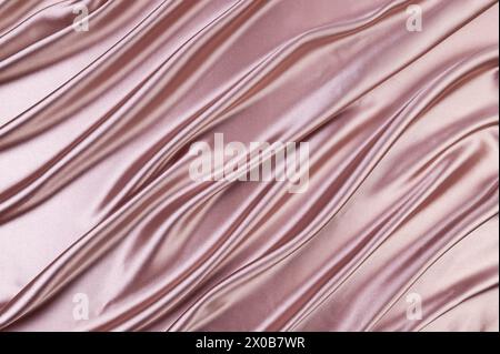 Luxury pink beige satin background. Soft and elegant silk fabric. Flowing waves textile. Top view. Stock Photo