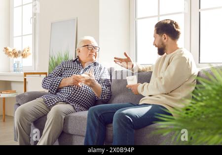 Familial connection family old father adult son sitting on sofa talking happy fatherhood. Family connection father and son heartwarming fatherhood Stock Photo