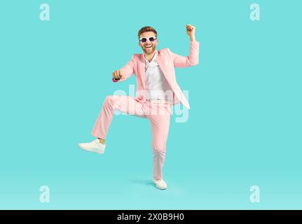Happy, funny, joyful young man in pink party suit dancing on bright blue background Stock Photo
