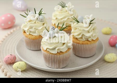 Tasty Easter cupcakes with vanilla cream and candies on table Stock Photo