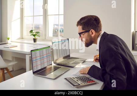 Business accountant sitting at his office desk, using laptops, and working with data sheets Stock Photo