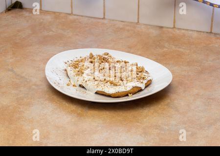 A homemade carrot cake dessert, with a creamy base topped with a crunchy garnish of walnuts and cinnamon on a classic white plate against the backdrop Stock Photo