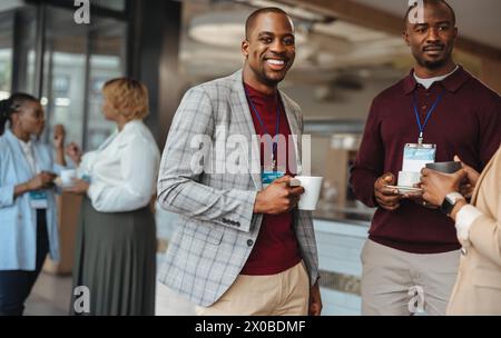 Two cheerful male professionals with name tags enjoying a light-hearted chat over coffee during a break at a business conference, portraying networkin Stock Photo