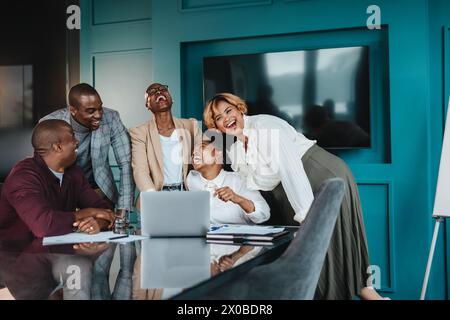 Colleagues in a boardroom have a successful business meeting. Business men and women collaborate using laptops, tablets, and computers. The group is h Stock Photo