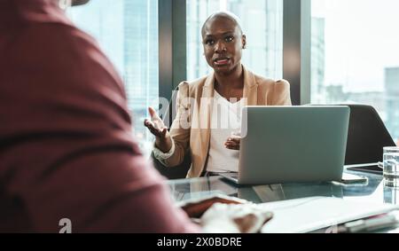 Professionals having a meeting in a corporate office. Two businesspeople, a man and a woman, discuss work at a desk. They are focused on laptops and t Stock Photo