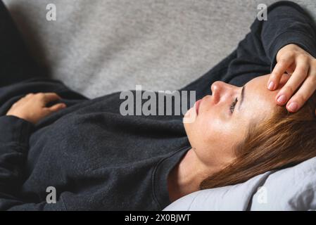 Young adult depressed woman lying down on a sofa at home, lying on back and looking up. Post-traumatic stress disorder. Stock Photo
