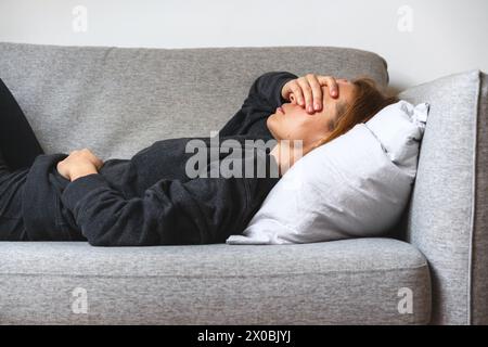 Unhappy despaired depressed woman lying on the sofa and covering eyes with her hand. Stock Photo