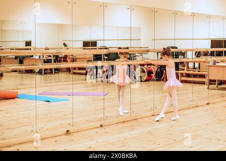 a girl in a tutu warming up on the barre in front of a mirror in a ballet studio Stock Photo