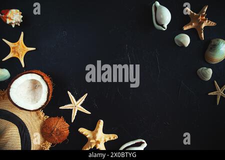 Straw hat, coconut, starfish and seashells on a black background. Summer background, free space for decoration, flat lay. Stock Photo