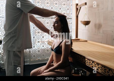 Professional masseur male doing massage head and shoulder for young woman in spa salon by window. Pretty female getting head massage by masseur in Stock Photo