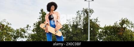 A young African American woman with curly hair gracefully stands on a skateboard in a vibrant park setting. Stock Photo