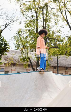 A young man with curly hair is skillfully riding a skateboard on top of a ramp in a skate park, showcasing his impressive tricks and maneuvers. Stock Photo
