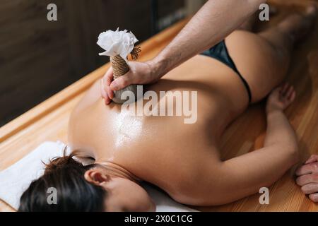 High-angle view of relaxed young woman lying with closed eyes receiving herbal bolus bags massage. Closeup hands of Ayurveda massage therapist Stock Photo