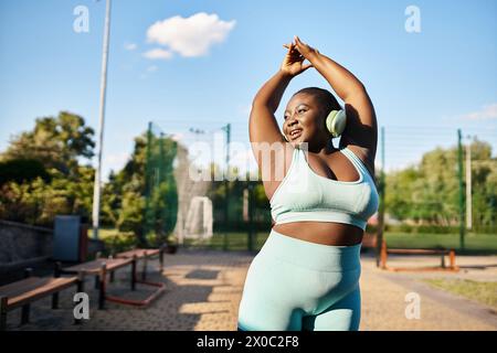 Curvy African American woman in sports bra top stretches her arms outdoors, promoting body positivity and fitness. Stock Photo