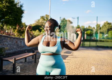 An African American woman in a sports bra and leggings flexes her muscles confidently outdoors. Stock Photo