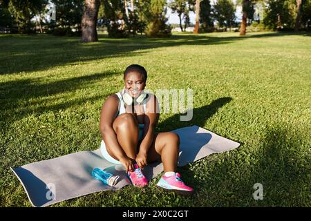 A curvy African American woman in sportswear sitting on a towel, enjoying the outdoors in a peaceful and serene setting. Stock Photo