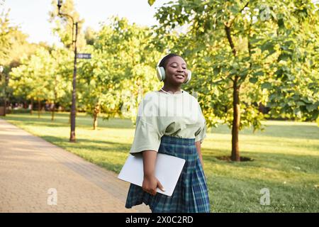 A plus size African American woman in casual attire walks confidently on a park sidewalk in summer. Stock Photo