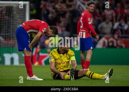 The captain of Borussia Dortmund, Emre Can, recovers on the grass from a foul while Cesar Azpilicueta (L), a Spanish player from Atletico Madrid, and Rodrigo de Paul (background) look on during the match for the quarterfinals of the UEFA Champions League played at the Metropolitan Stadium in Madrid. First leg match for the quarterfinals of the UEFA Champions League played at the Metropolitan Stadium in Madrid between Atlético de Madrid and the German Borusia Dormund with a score of 2 goals to 1 for the local team with goals from Rodrigo de Paul (4' ) and Samuel Lino (32') for the ATM and Sebas Stock Photo