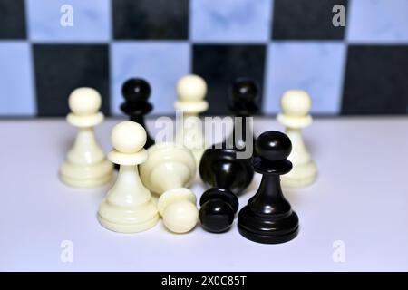 In the picture, chess pieces of pawns of two colors stand and lie mixed up on a white table. Stock Photo