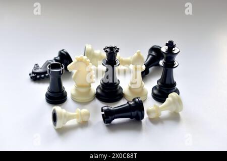 In the picture, chess pieces of two colors are standing and lying mixed on a white table. Stock Photo