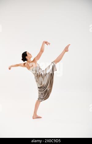A graceful young woman in a long and shiny silver dress elegantly dances in a studio setting against a white background. Stock Photo