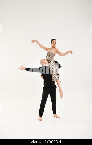 A young man in black carries a young woman in a dress while dancing gracefully, showcasing acrobatic elements. Stock Photo