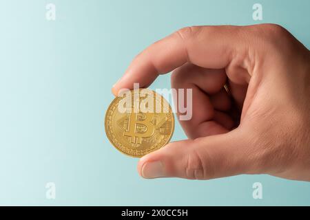 Hand of man holds Bitcoin cryptocurrency gold coin on blue background. Minimal investing concept. Stock Photo