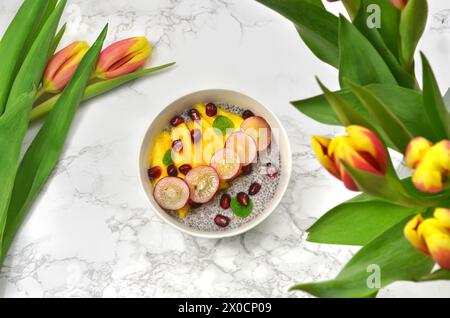 Chia seeds dessert with fruits surrounded with yellow and red tulips. Top view. Stock Photo