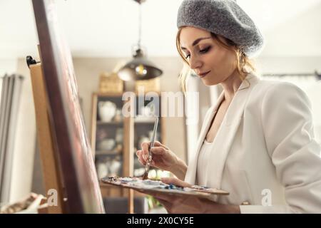 Beautiful female painter enjoying while painting in home art studio. Woman Artist Works on Abstract acrylic painting in the art studio. Stock Photo