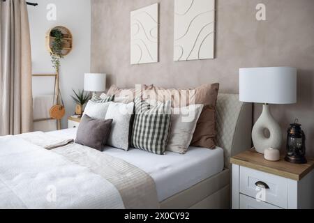 Modern bedroom interior, white blanket, lots of pillows and stylish night lamps. Stock Photo